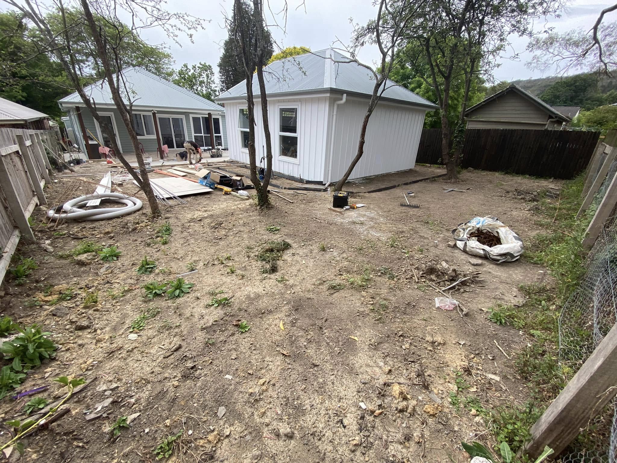 Rear yard during construction, with bare soil around the house and outbuilding.